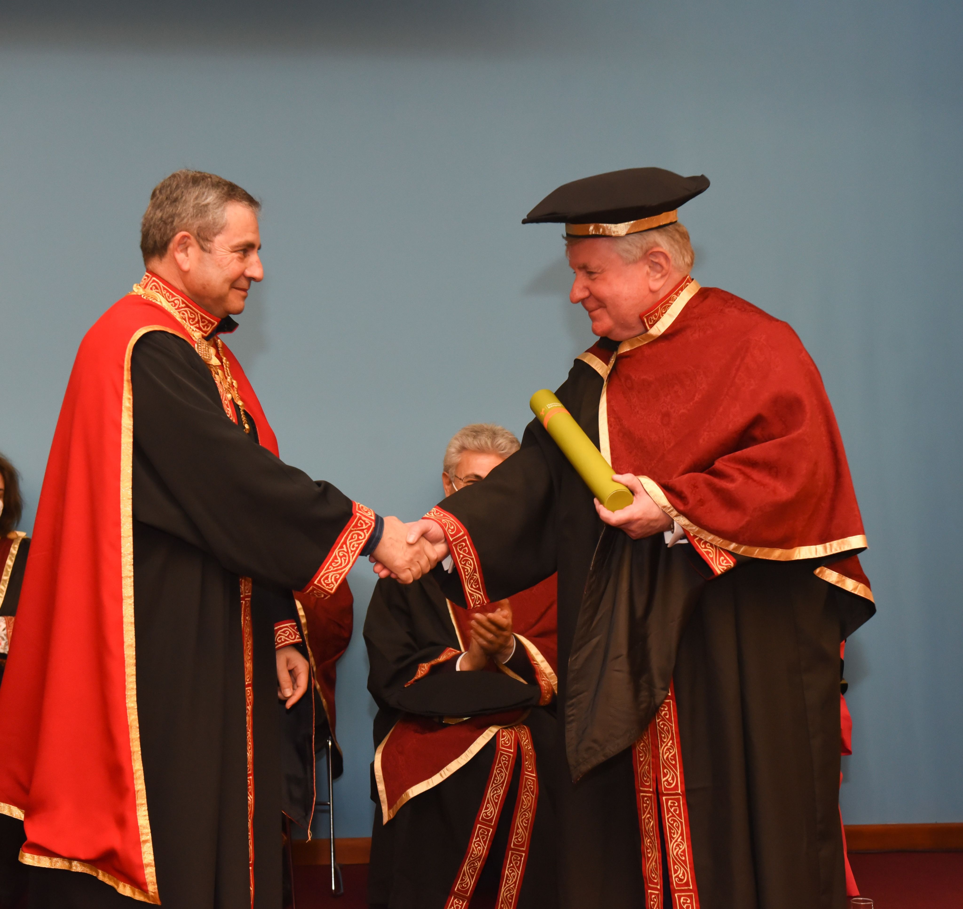 Two men in red robes shaking hands at a graduation ceremony