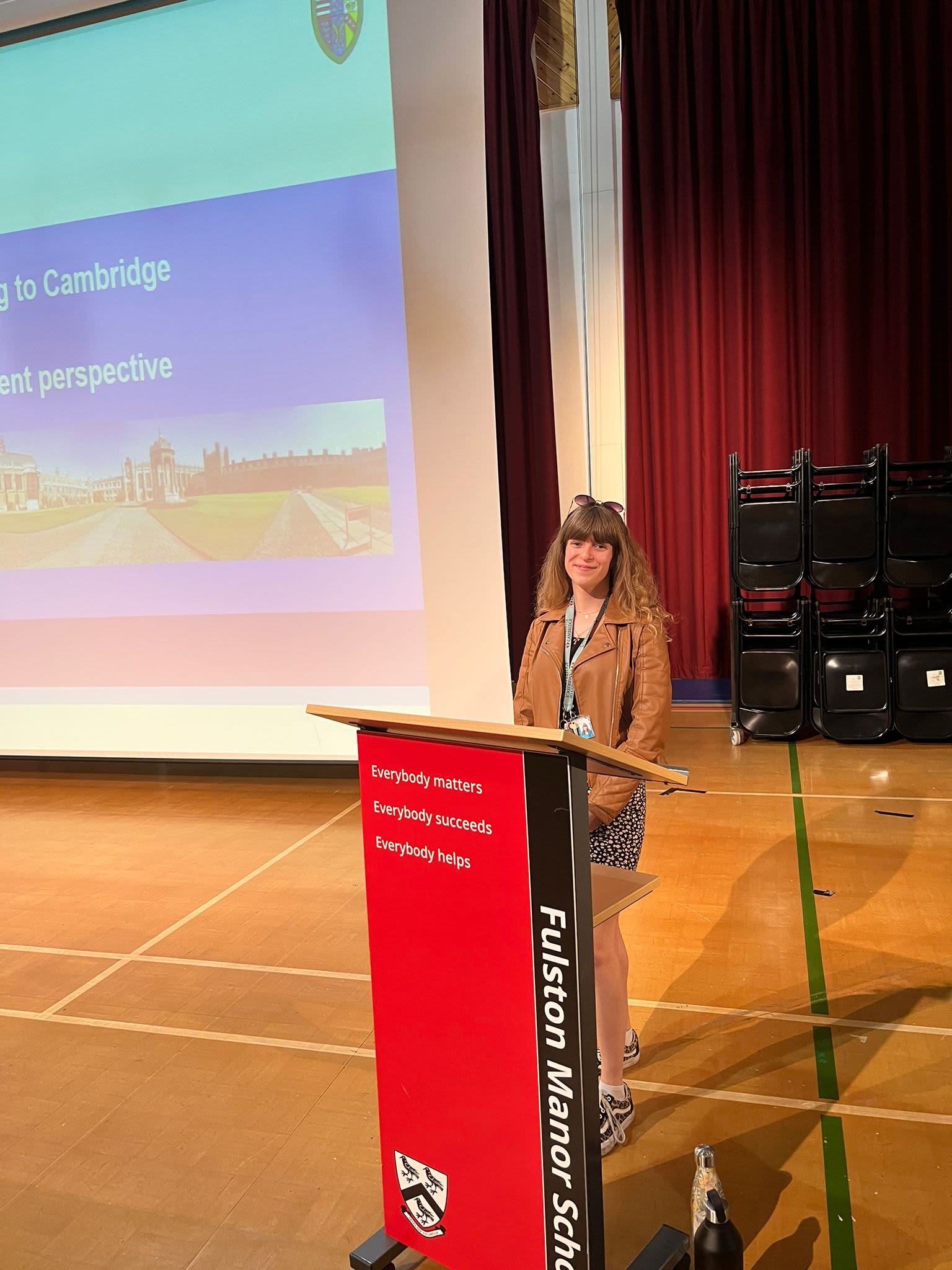 A woman standing at a podium on stage presenting in front of a powerpoint screen