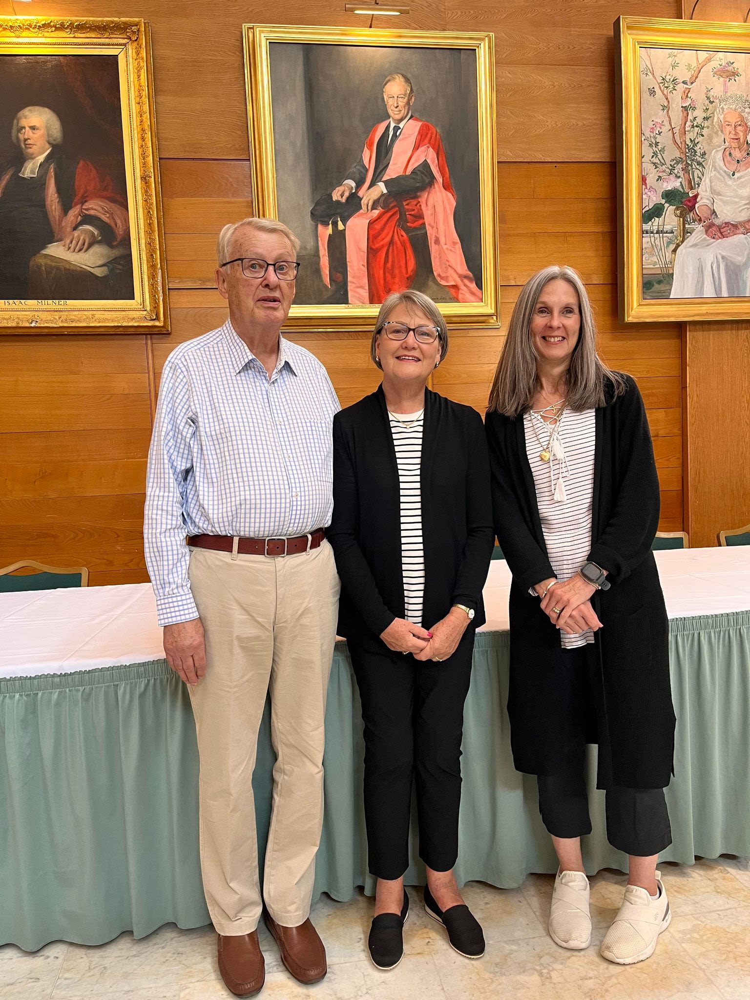 Three people in front of three portraits on the wall